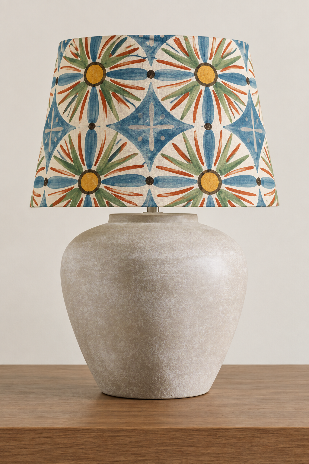 A pendant lampshade with a handwoven raffia body and long natural fringe, suspended against a soft beige background.