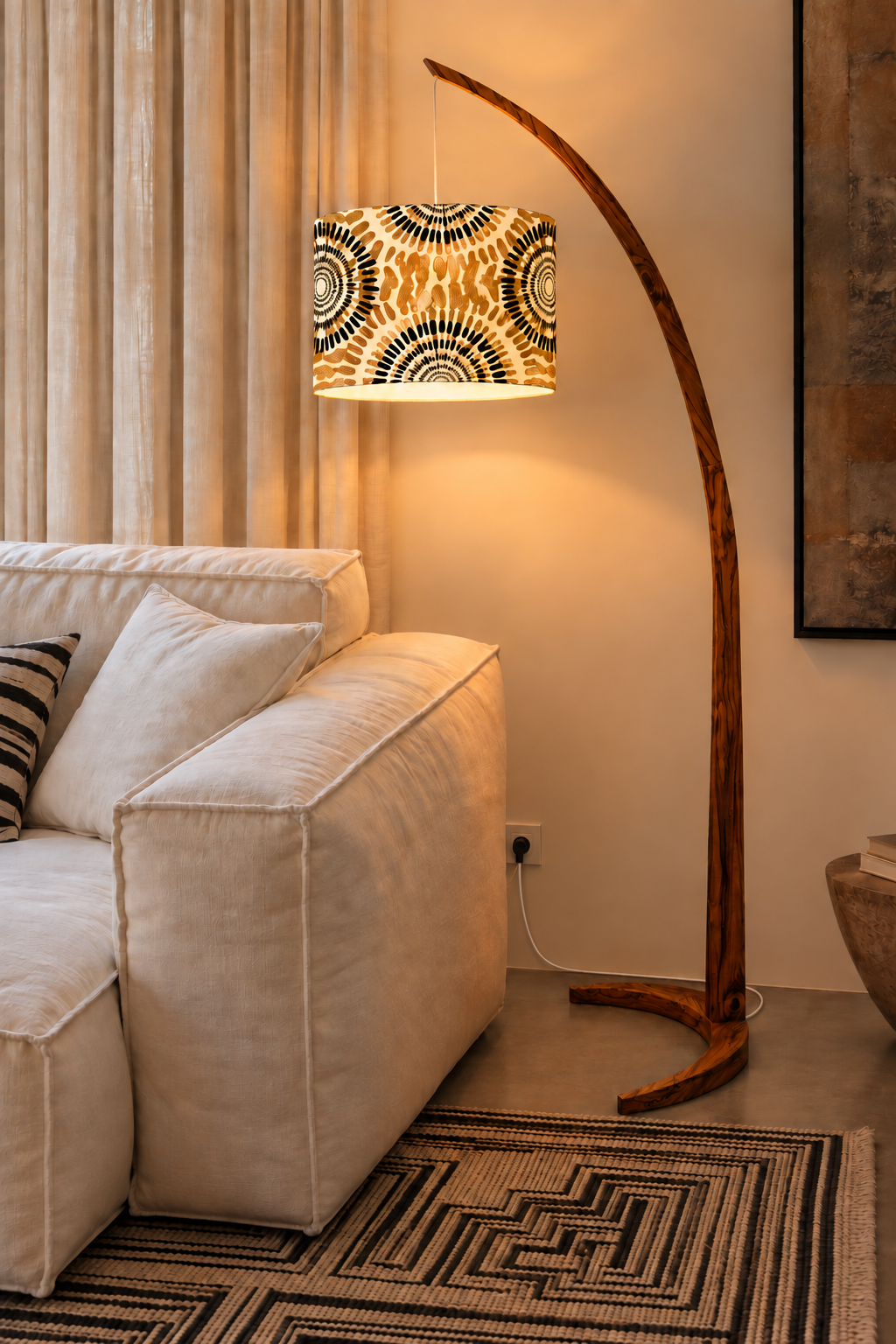 LAIMA Floor Lamp in solid mkongo wood with a sweeping arc and printed drum shade, casting warm ambient light over a white sofa in a calm living room with linen curtains and a woven rug