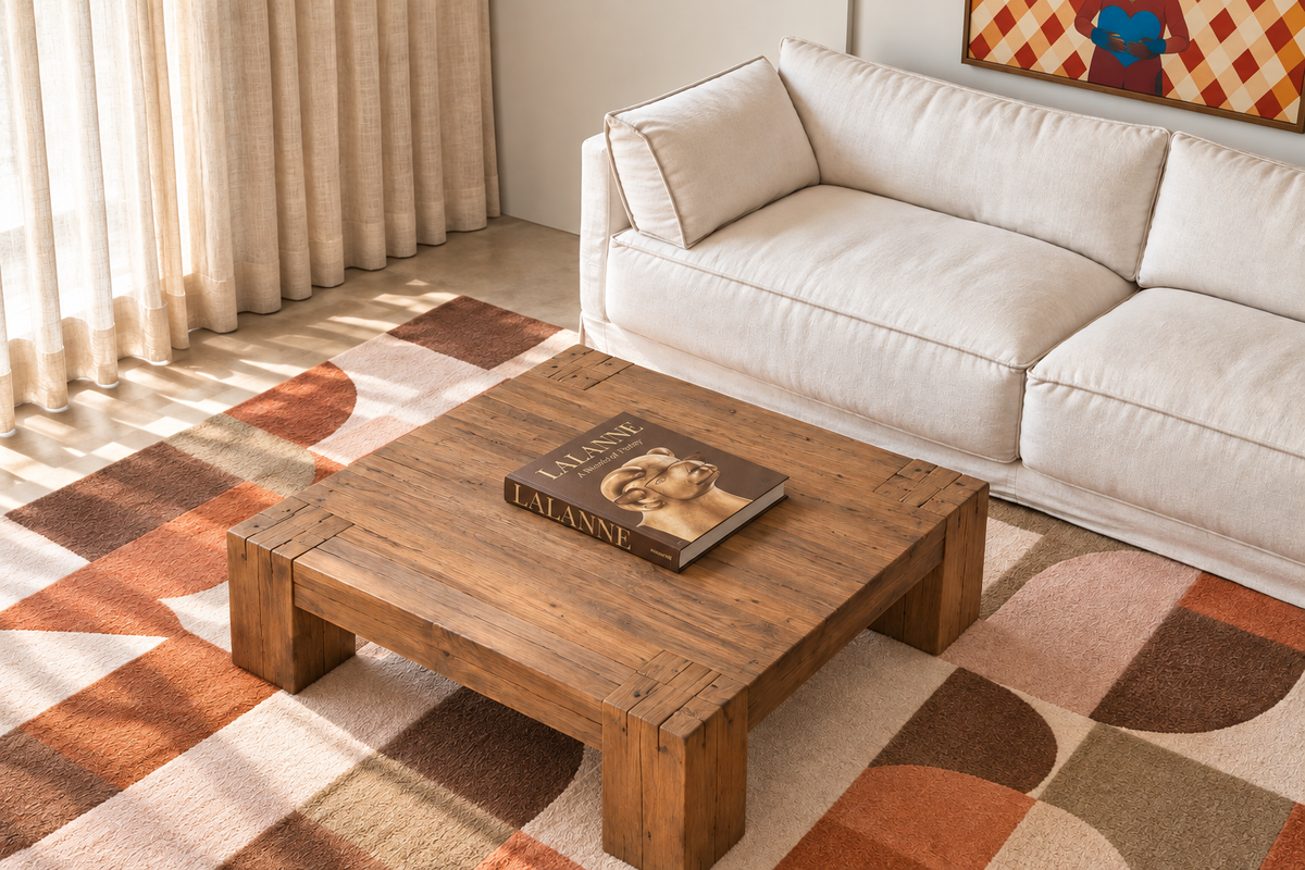 SUBA Coffee Table in solid reclaimed timber with thick block legs and natural grain markings, styled in a bright living room with a white sofa, abstract patterned rug and a Lalanne art book on top