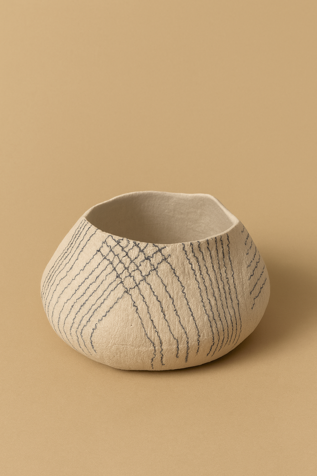 Ivory felt vessel with dark lines, sculptural and organic, placed against a sand-colored background