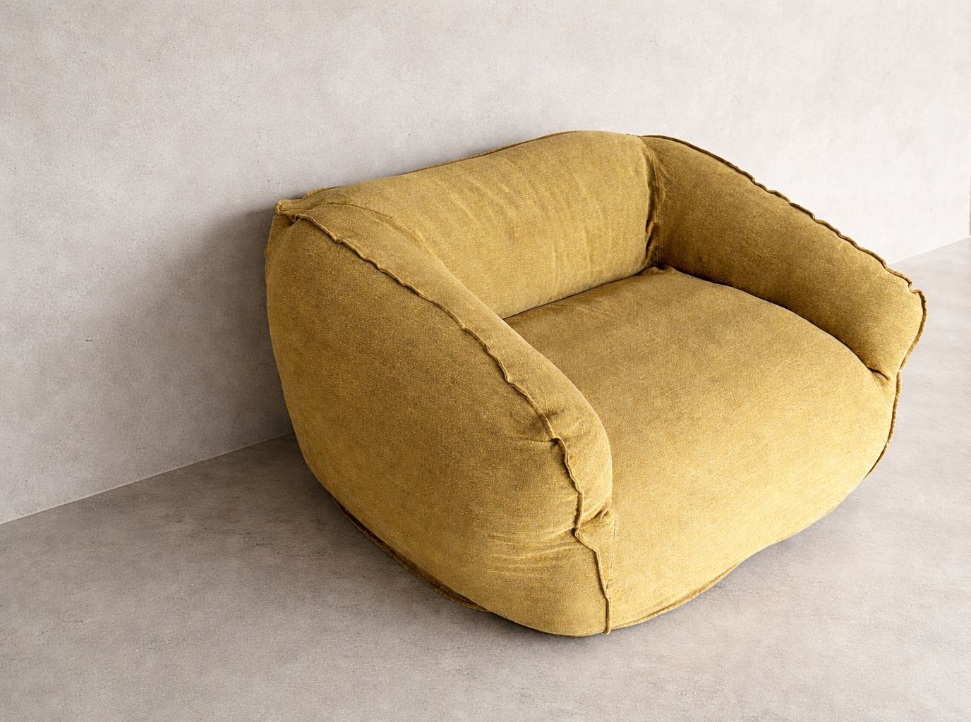 Cousin armchair upholstered in 100% natural linen with rounded back, curved arms and visible seam detailing, set against a mineral plaster wall in soft natural light.