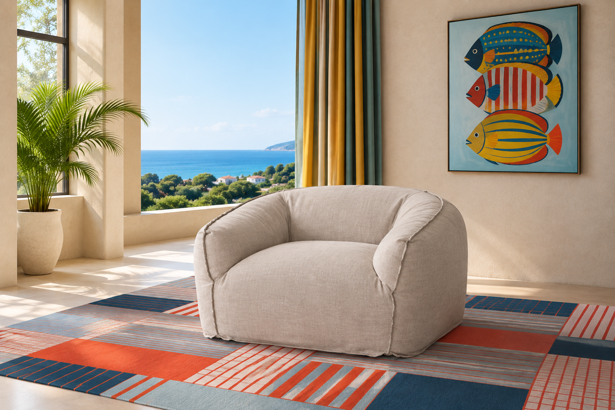 COUSIN Armchair in cream linen upholstery styled in a bright coastal living room with ocean views and a colourful fish art print