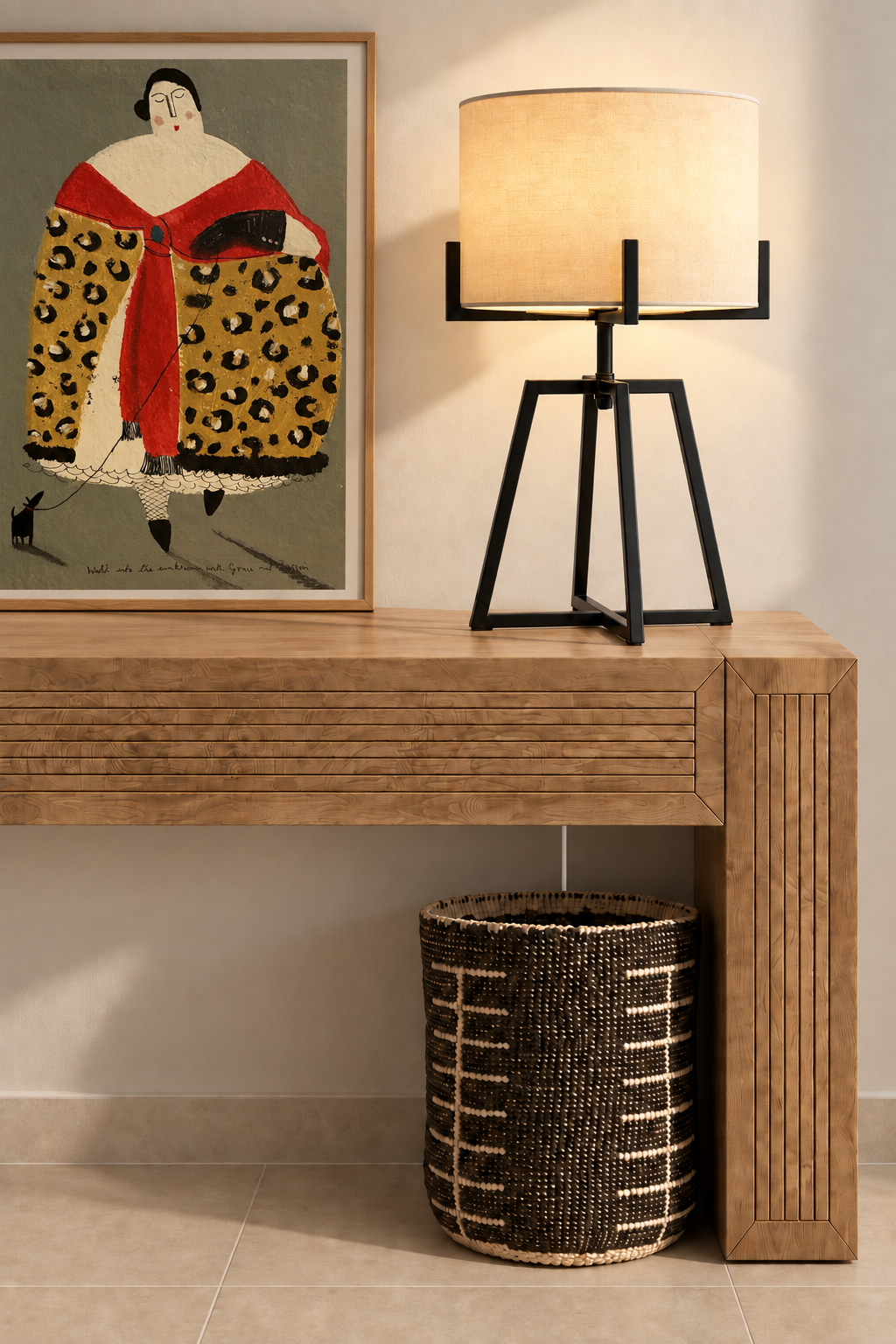 KIKAO Table Lamp with geometric powder-coated black steel base and cream drum shade, styled on a slatted teak console with a woven basket and a bold figurative art print
