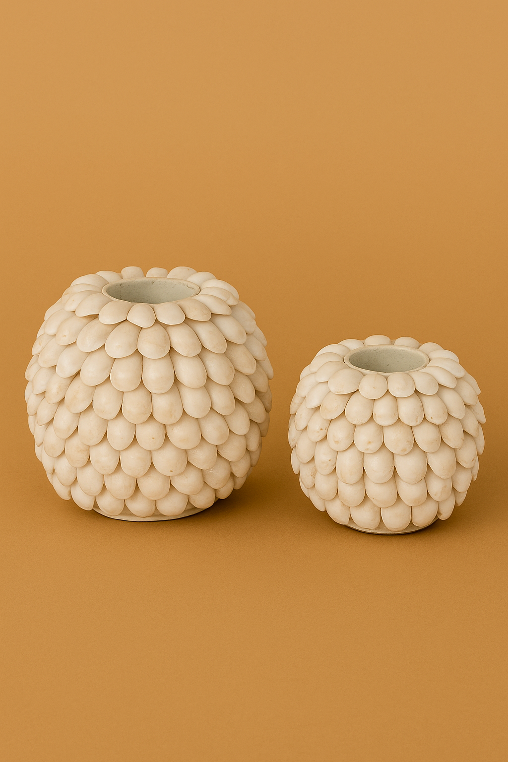 Two handmade candle holders covered in white shells, set against a camel background