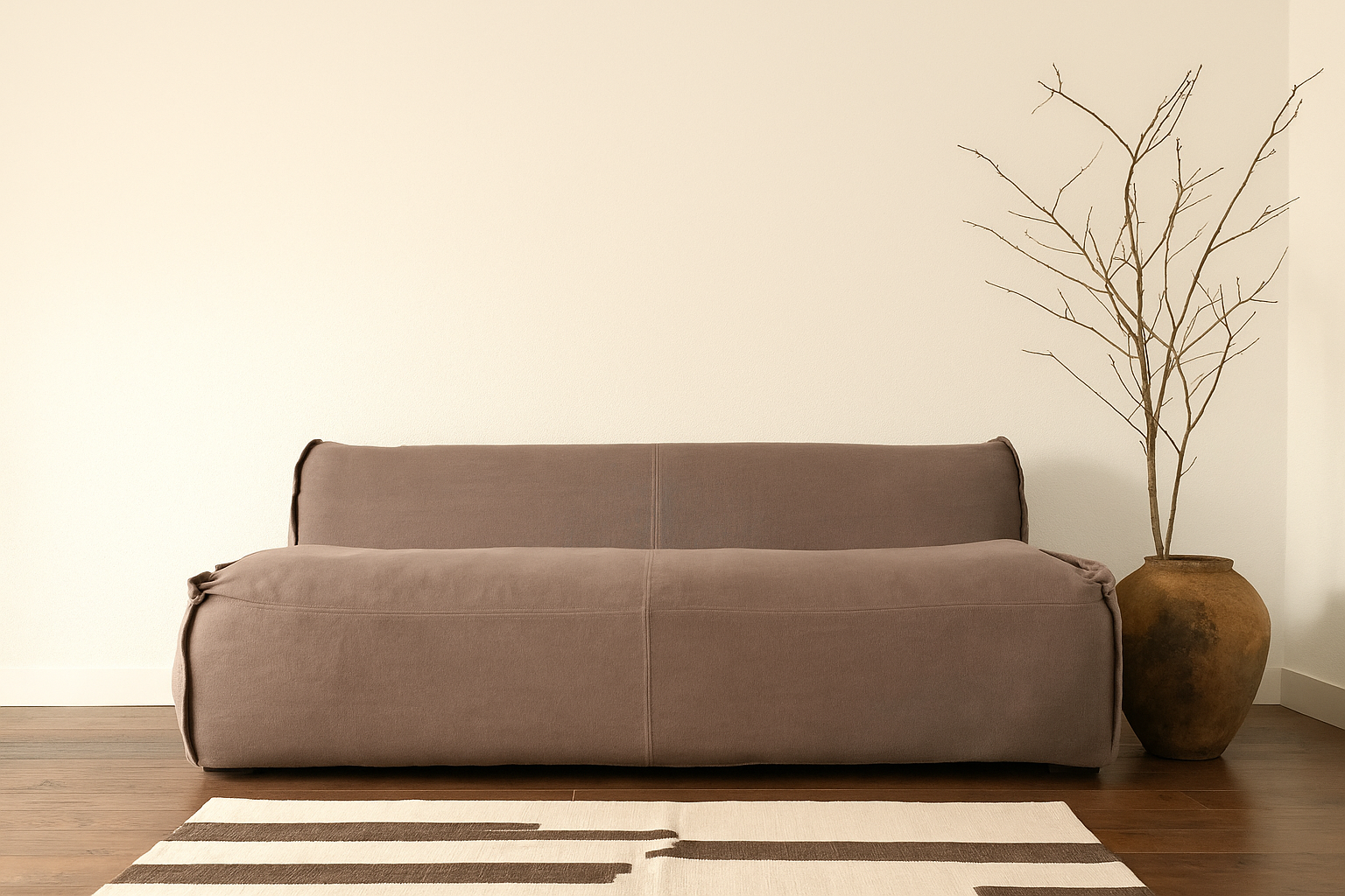 Low three-seater modern sofa in soft brown upholstery, styled on a cream rug with woven wall basket and neutral background