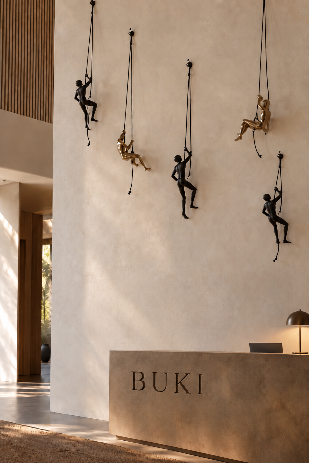 Solid brass climbing man wall sculpture suspended from rope, with a dark textured finish.