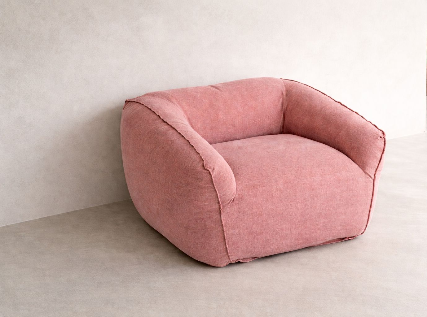 Cousin armchair upholstered in 100% natural linen with rounded back, curved arms and visible seam detailing, set against a mineral plaster wall in soft natural light.