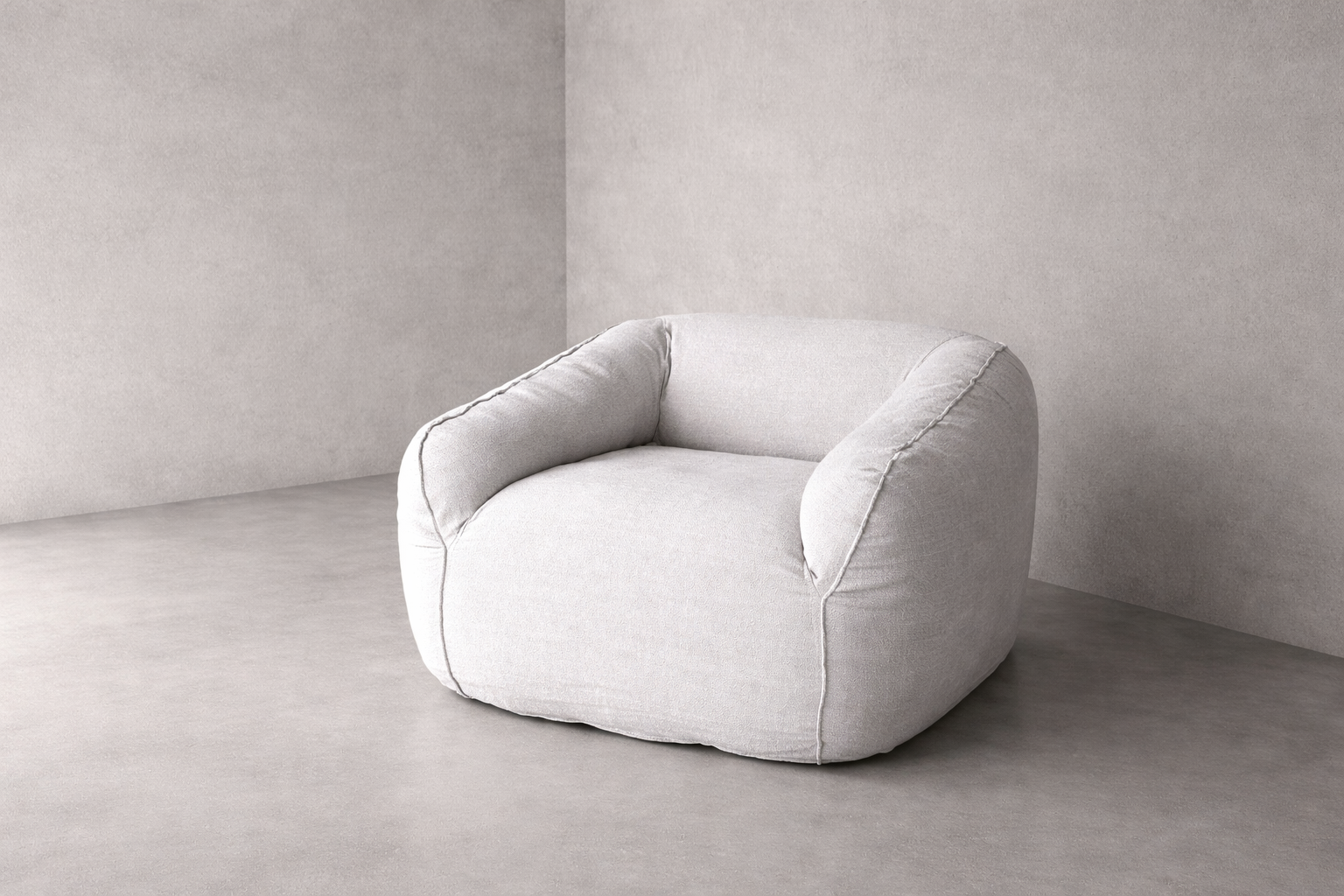 Cousin armchair upholstered in 100% natural linen with rounded back, curved arms and visible seam detailing, set against a mineral plaster wall in soft natural light.