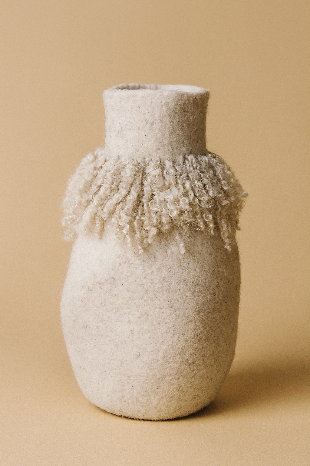 Textured felt vase with fringe detail on a beige background