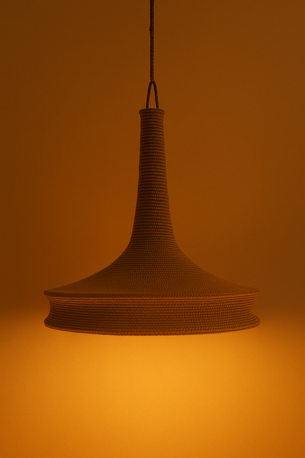 A photograph features a pendant light made from handwoven nilon thread in a wide, flared silhouette, hanging against a warm-toned background.