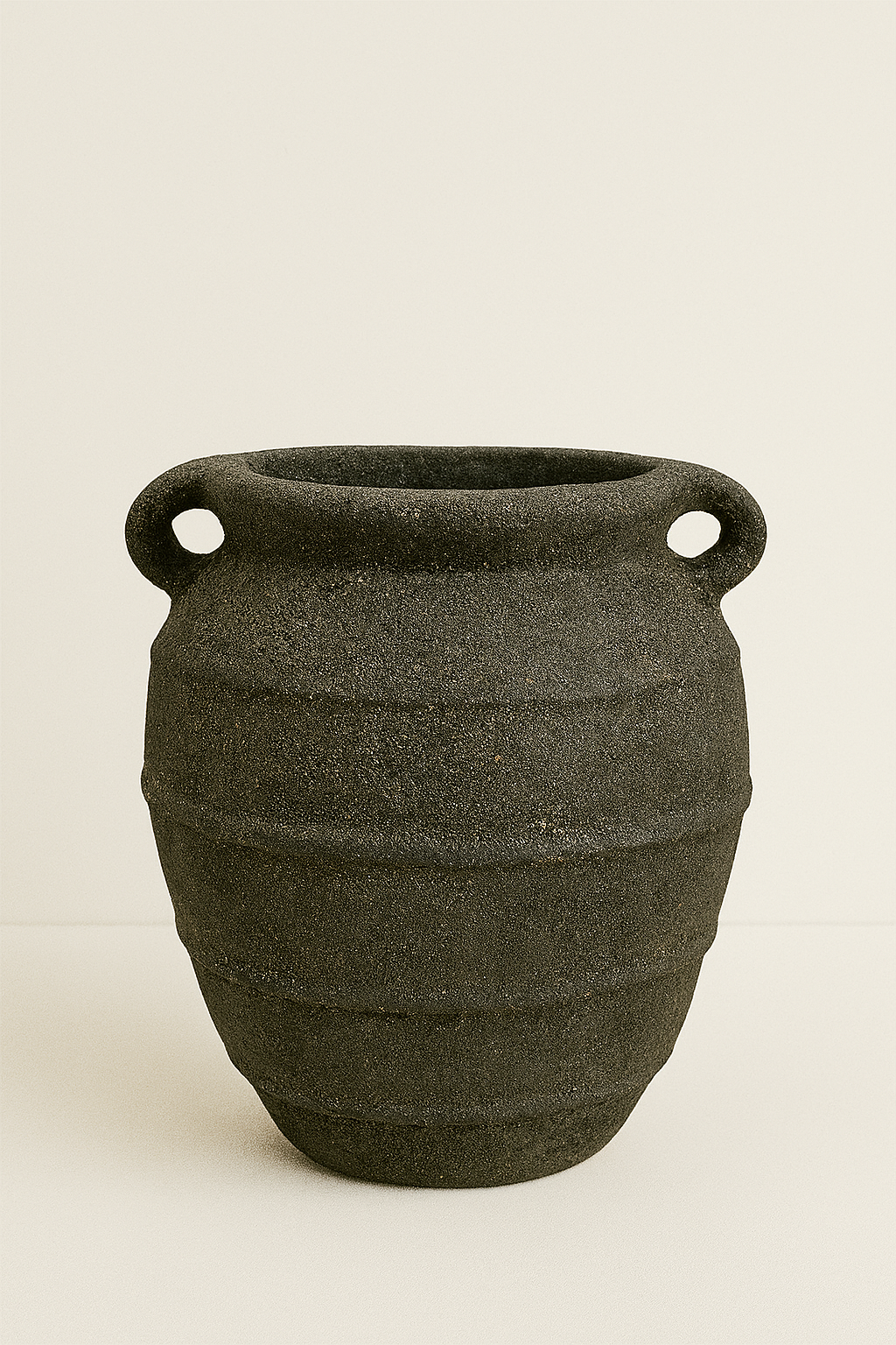 Black stoneware pot with two handles on a beige background