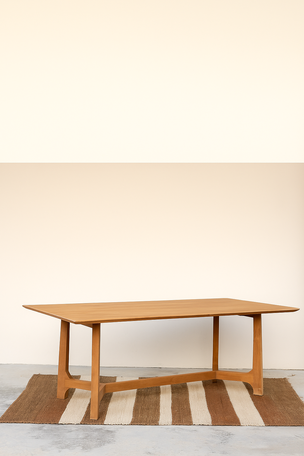 A rectangular wooden dining table with tapered legs and a sculptural crossbar base, placed on a striped rug against a soft neutral background.