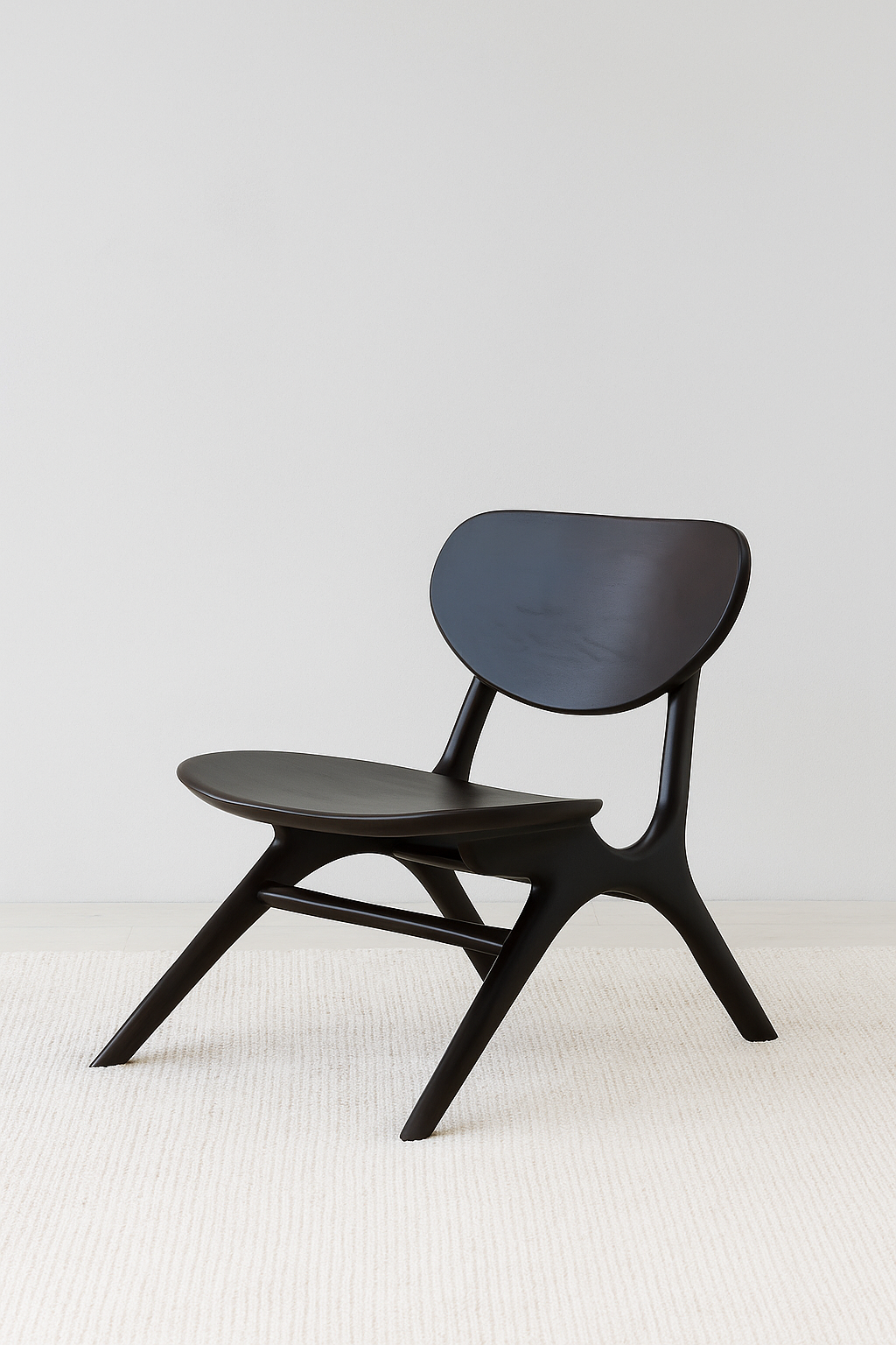 A modern lounge chair crafted from dark wood with a sculptural silhouette, featuring a wide curved seat and backrest, set against a soft grey wall with a textured neutral rug underneath.